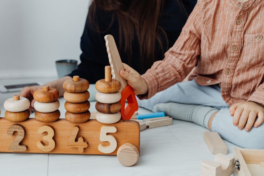 A child in brown outfit playing with wooden educational toys on a white surface.