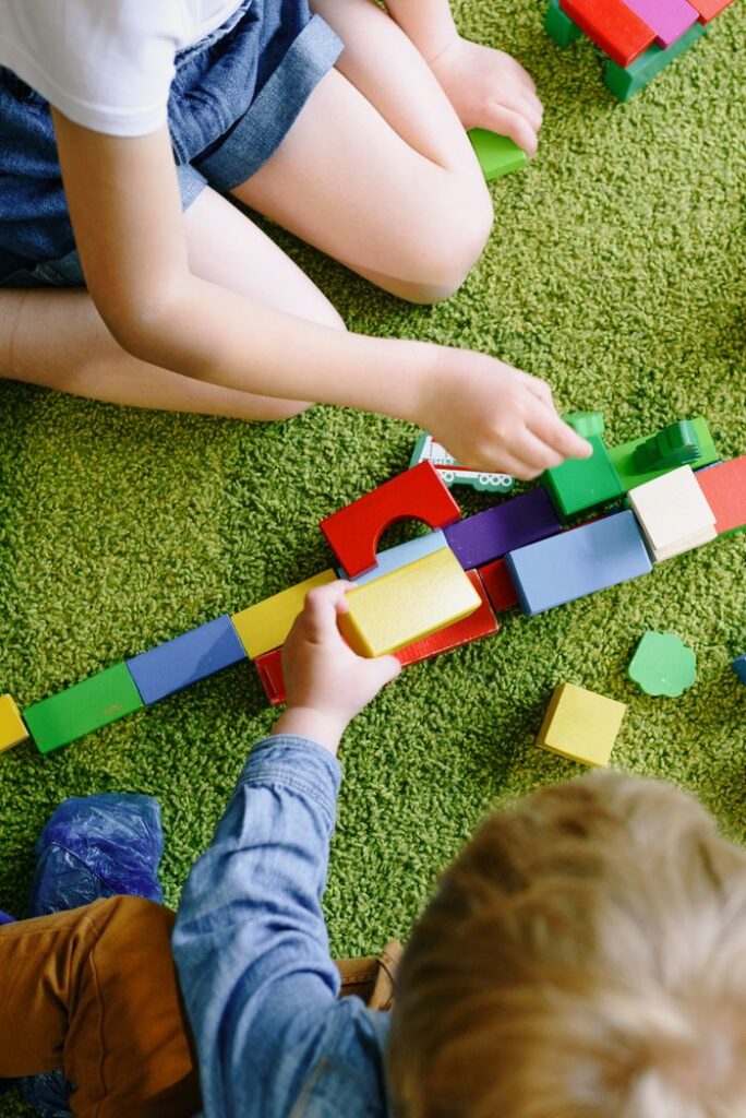 Children engaged in playful activities with vibrant blocks on a green carpet.